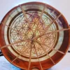 A large circular wooden bowl with a flower of life design.