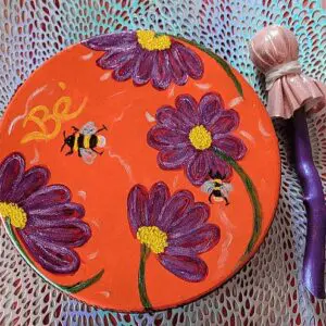 A round box with purple flowers and bees painted on it.