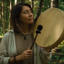 A woman holding a drum in the woods